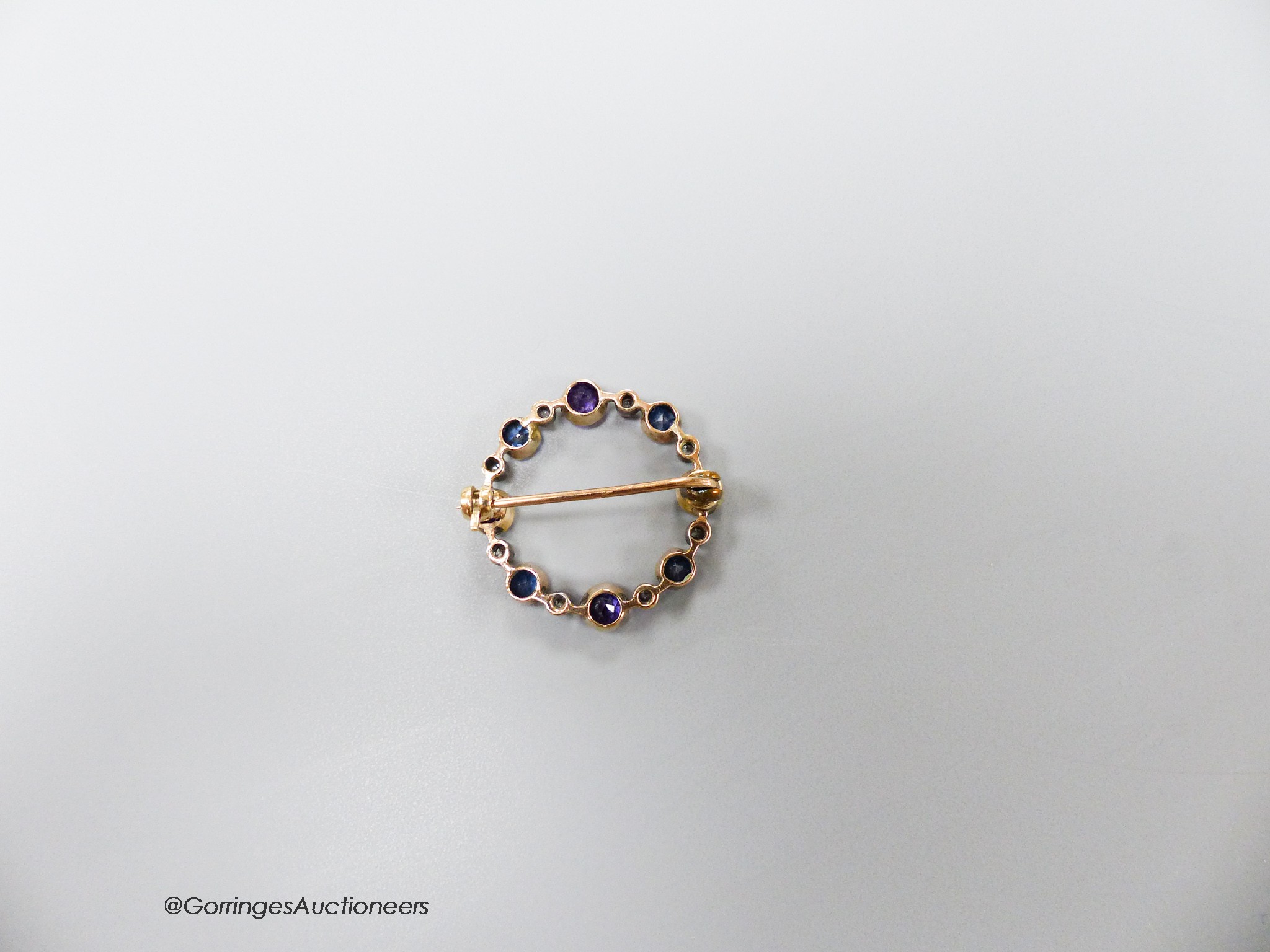 An early 20th century yellow metal, amethyst, sapphire and diamond chip set openwork circular brooch, 27mm, gross 3.9 grams.